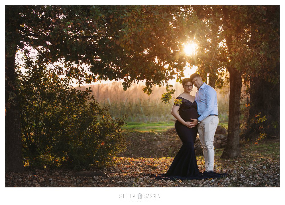 Maternity shoot couple in a forest with sunbeams coming through the leaves of the treee
